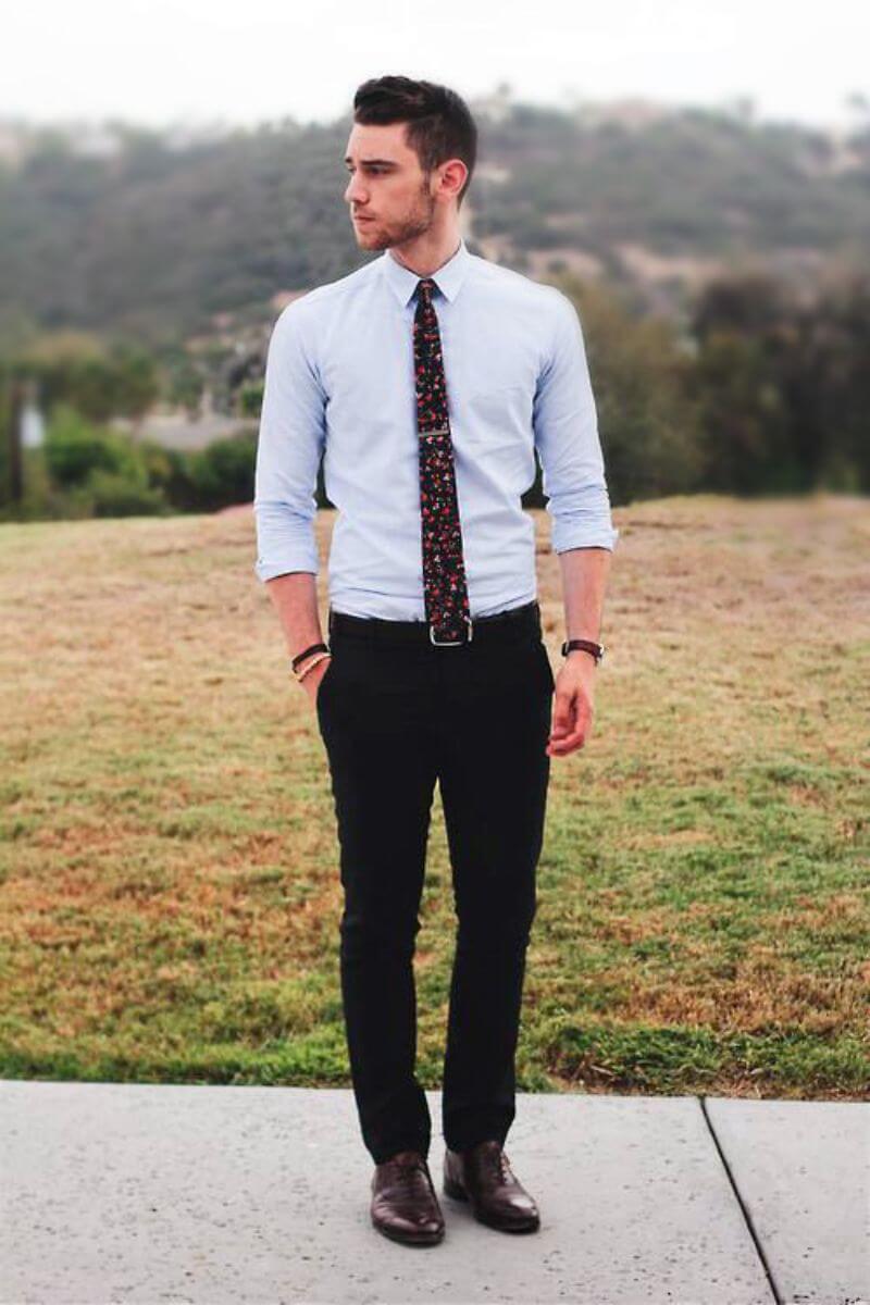 Young, white man with dark hair and a short beard wearing black trousers, a pale blue shirt and a floral tie.